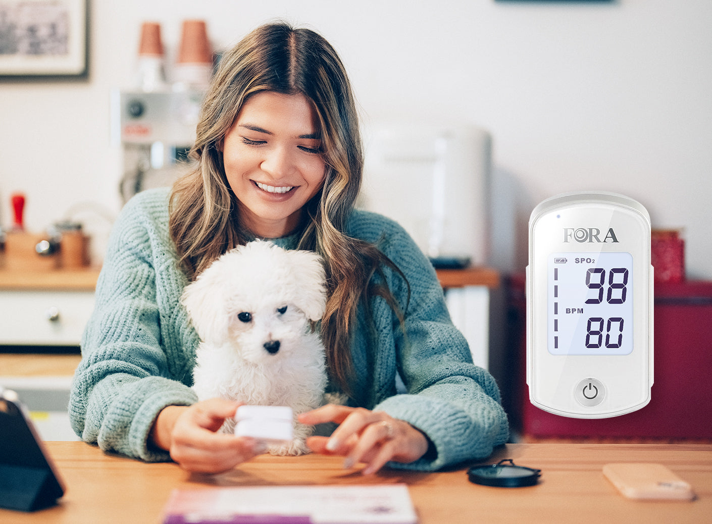 A smiling woman in a light blue sweater using a FORA pulse oximeter at home, holding a small white dog, with the device screen showing 98% SpO2 and 80 BPM
